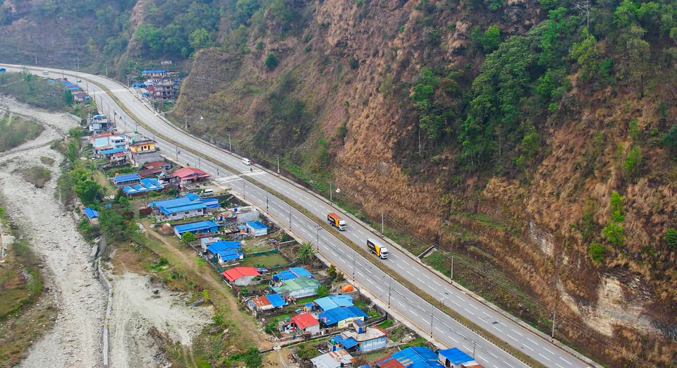 Aerial view of Darshan Transport trucks passing a hillside village